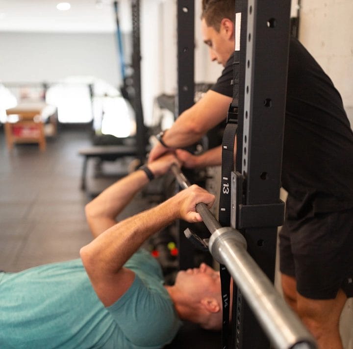 man in blue shirt train do benchpress with another man